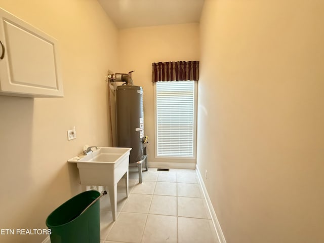 laundry room featuring water heater, baseboards, and light tile patterned flooring