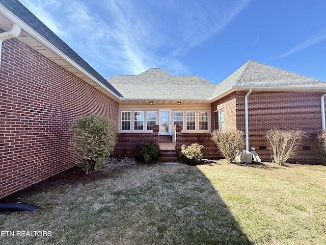 back of property featuring crawl space, roof with shingles, a lawn, and brick siding