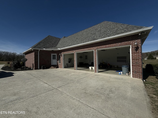 rear view of property featuring driveway, a shingled roof, an attached garage, and brick siding