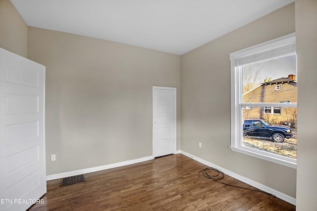 empty room with baseboards, visible vents, and dark wood finished floors