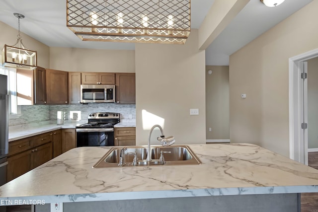 kitchen featuring decorative light fixtures, backsplash, appliances with stainless steel finishes, a sink, and light stone countertops