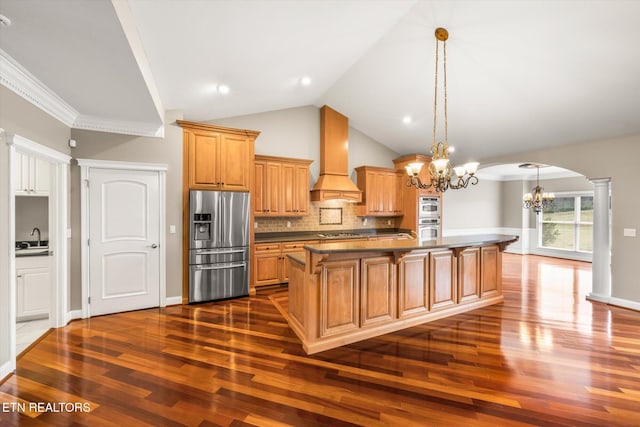 kitchen with arched walkways, stainless steel refrigerator with ice dispenser, dark countertops, cooktop, and custom range hood