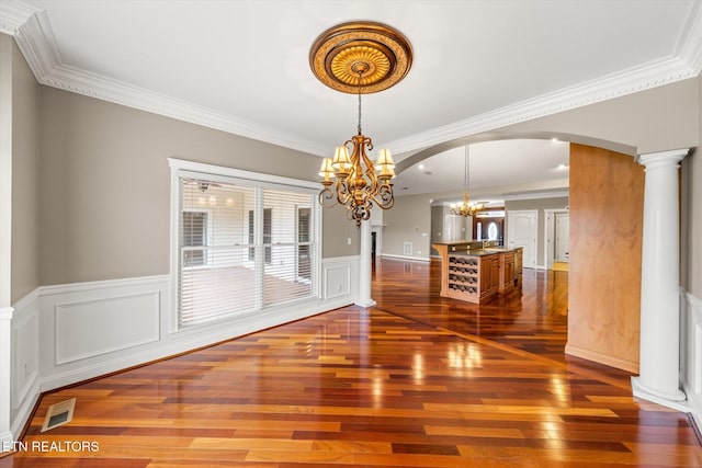 unfurnished dining area with arched walkways, dark wood-style flooring, visible vents, decorative columns, and an inviting chandelier