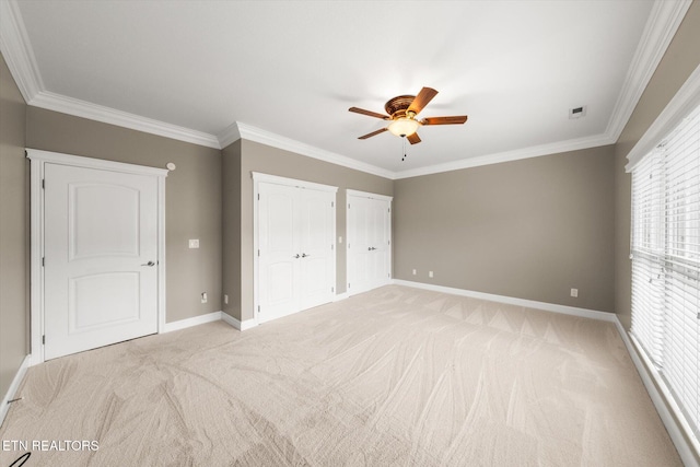 unfurnished bedroom with baseboards, ornamental molding, multiple closets, and light colored carpet