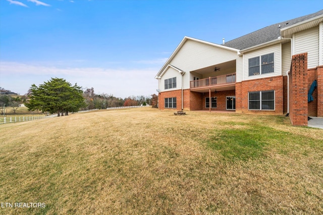 rear view of house featuring ceiling fan, a lawn, and brick siding