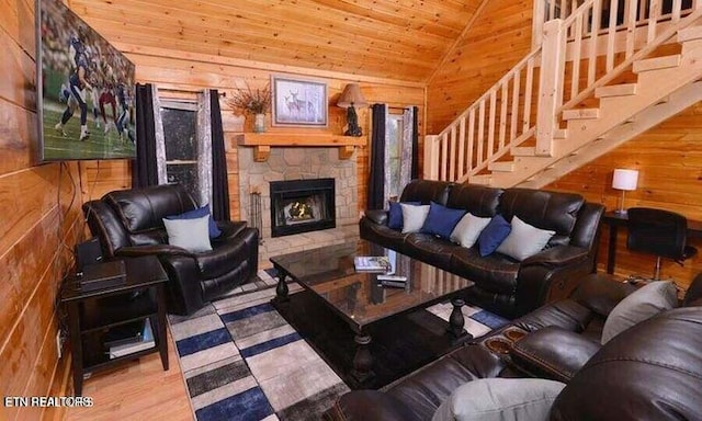 living area with lofted ceiling, wood ceiling, a stone fireplace, wooden walls, and stairs