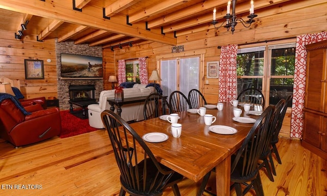 dining area featuring a stone fireplace, wooden walls, wood finished floors, a wealth of natural light, and beam ceiling