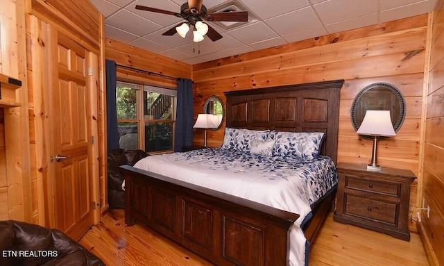 bedroom featuring light wood-style floors, a drop ceiling, and wood walls