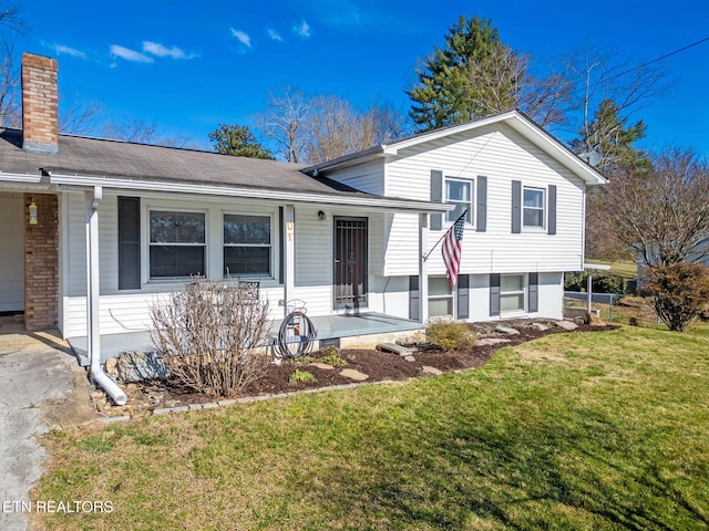 tri-level home with covered porch, brick siding, a chimney, and a front yard