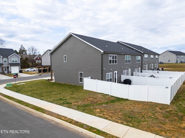 view of side of home featuring a lawn, fence, and a residential view