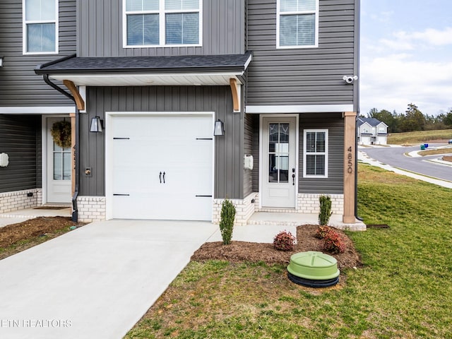 view of exterior entry with a garage, concrete driveway, roof with shingles, a yard, and board and batten siding