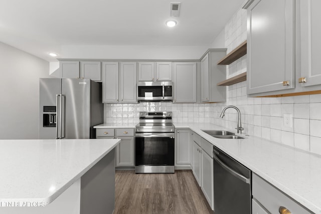 kitchen featuring tasteful backsplash, gray cabinets, stainless steel appliances, open shelves, and a sink