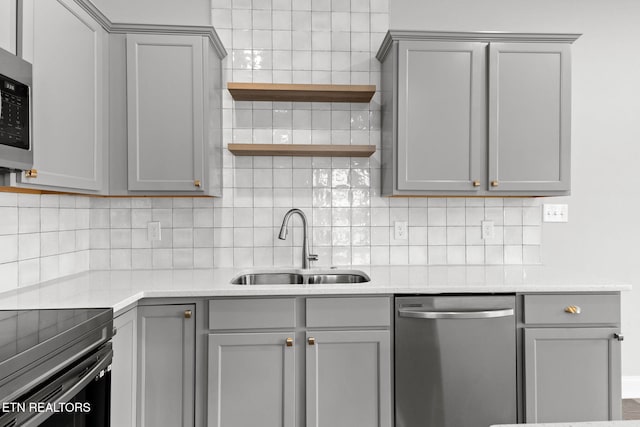 kitchen with appliances with stainless steel finishes, a sink, gray cabinets, open shelves, and backsplash