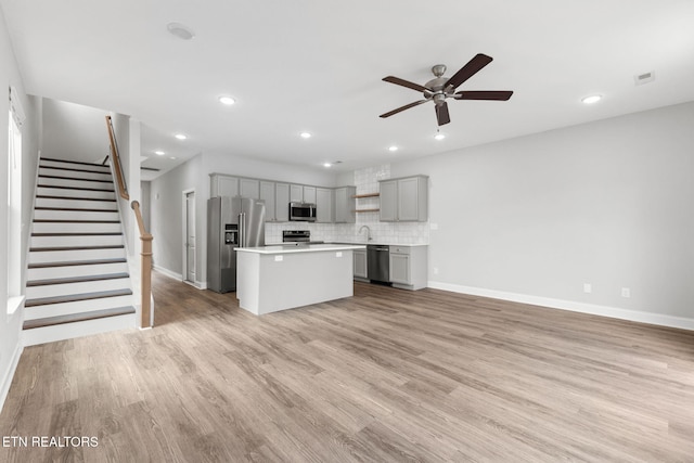 kitchen with a center island, stainless steel appliances, light countertops, gray cabinetry, and light wood-style floors