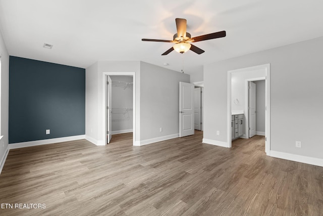 unfurnished bedroom with baseboards, ceiling fan, wood finished floors, a spacious closet, and a closet