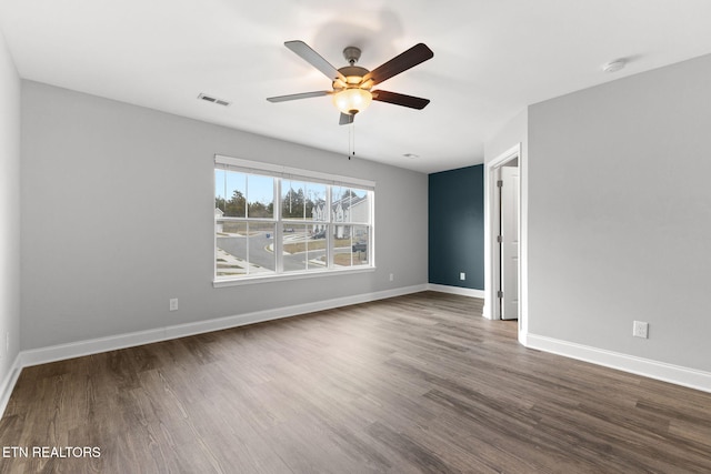 empty room with dark wood-type flooring, a ceiling fan, visible vents, and baseboards