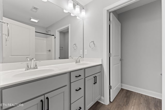 bathroom with double vanity, baseboards, a sink, and wood finished floors