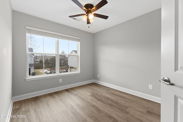 empty room featuring ceiling fan, wood finished floors, visible vents, and baseboards