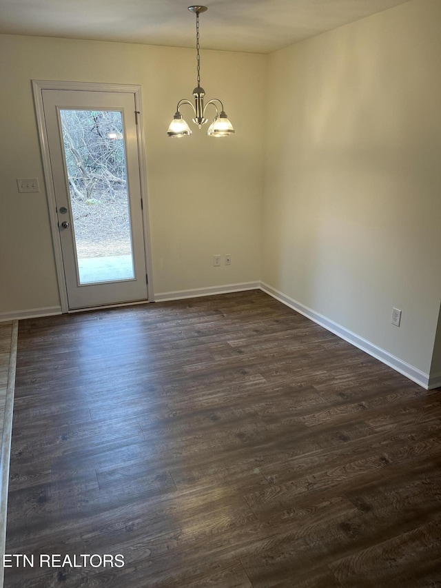 spare room with an inviting chandelier, dark wood-type flooring, and baseboards