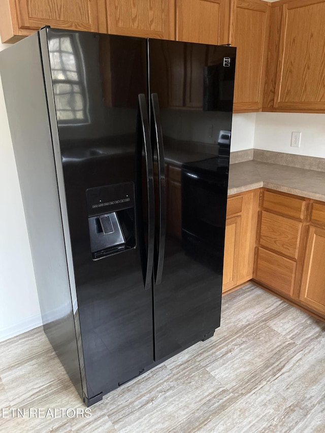 kitchen with black fridge with ice dispenser and light wood-type flooring