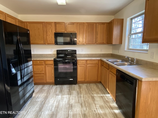 kitchen featuring brown cabinetry, a sink, black appliances, light countertops, and light wood-style floors