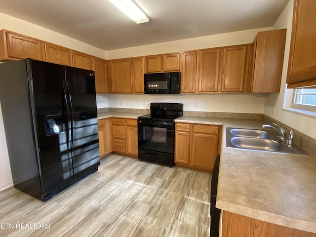 kitchen with light countertops, light wood-style floors, brown cabinetry, black appliances, and a sink