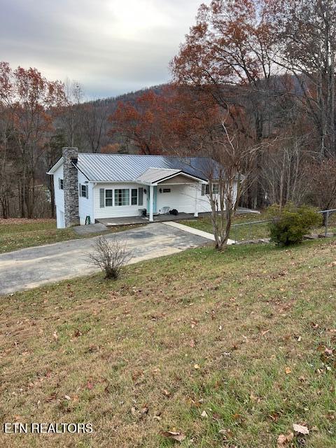 single story home featuring concrete driveway, metal roof, a front lawn, and fence