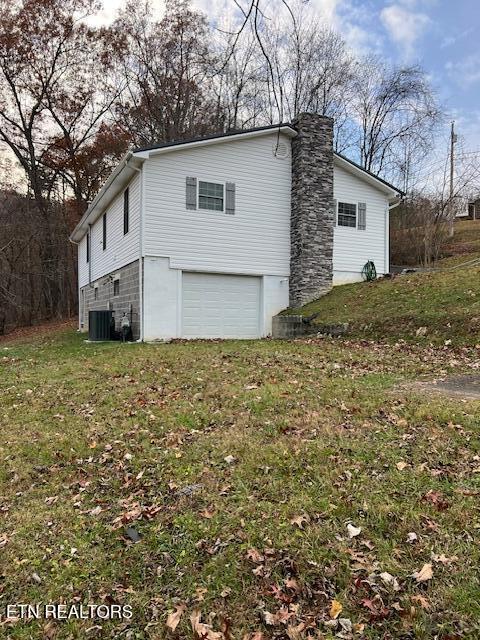 view of home's exterior with a chimney, an attached garage, and a lawn