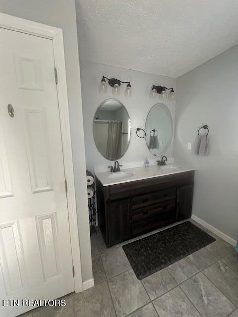 bathroom with a textured ceiling, double vanity, a sink, and baseboards