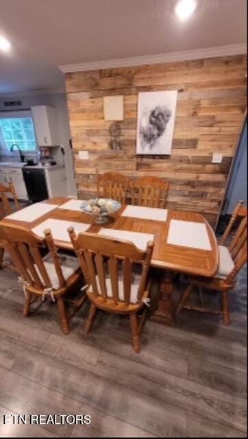 dining room with crown molding, wooden walls, and wood finished floors