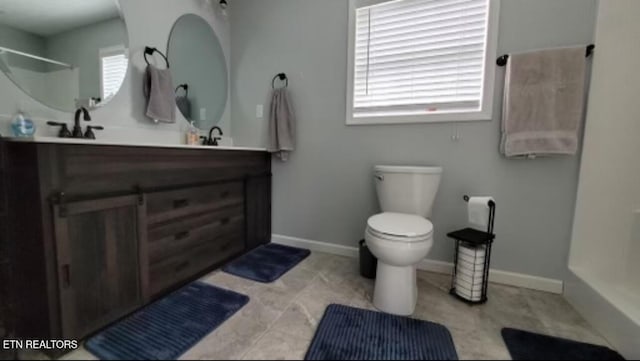 full bath with double vanity, baseboards, toilet, walk in shower, and a sink