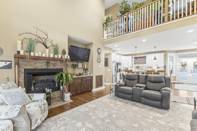 living area featuring a towering ceiling, baseboards, wood finished floors, and a stone fireplace