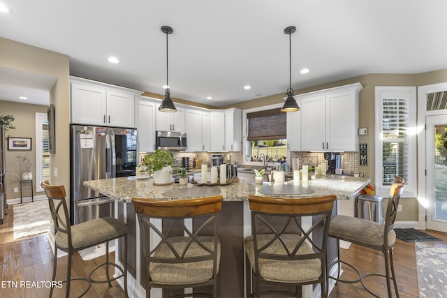 kitchen with appliances with stainless steel finishes, wood finished floors, white cabinetry, and decorative backsplash