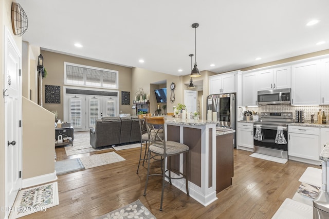 kitchen featuring wood-type flooring, decorative backsplash, appliances with stainless steel finishes, white cabinets, and a kitchen bar