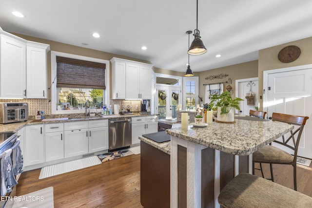 kitchen featuring tasteful backsplash, white cabinets, a kitchen island, a kitchen breakfast bar, and stainless steel dishwasher