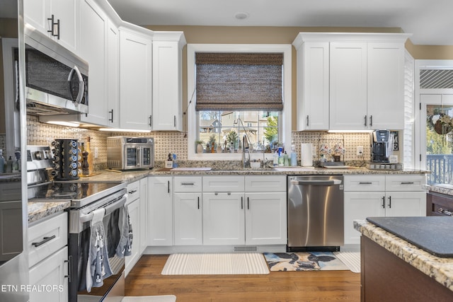 kitchen with wood finished floors, appliances with stainless steel finishes, a sink, and white cabinetry