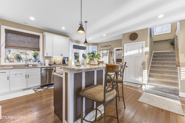 kitchen featuring a kitchen breakfast bar, a center island, stainless steel dishwasher, white cabinetry, and a sink