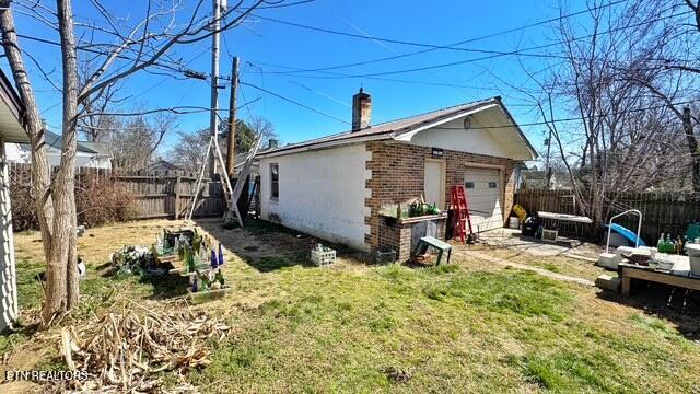 view of home's exterior with fence private yard, a garage, brick siding, a yard, and a chimney