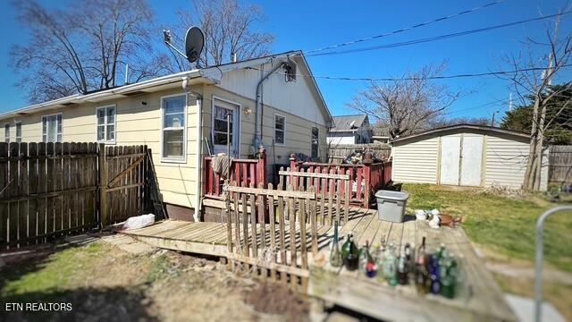 rear view of property with a deck, a storage unit, an outdoor structure, and fence