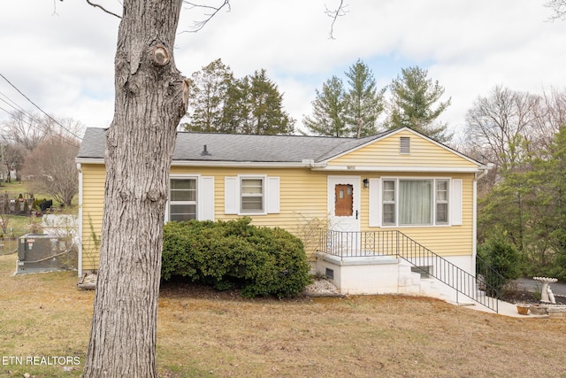 view of front of house with a shingled roof, a front lawn, and cooling unit