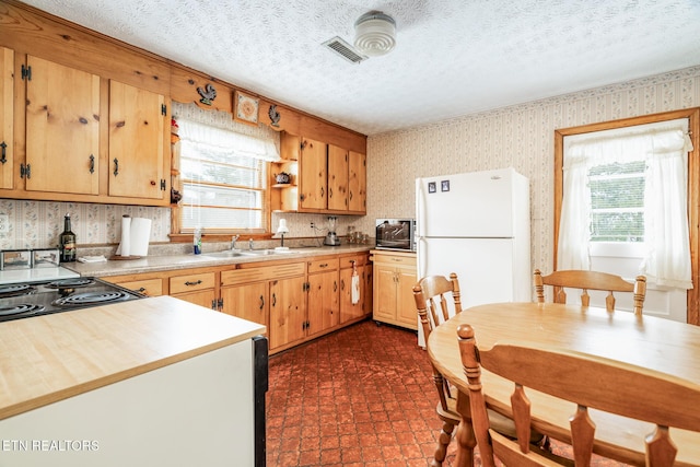 kitchen featuring a textured ceiling, a healthy amount of sunlight, freestanding refrigerator, and wallpapered walls