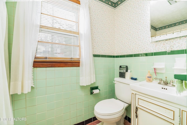 bathroom featuring wallpapered walls, wainscoting, toilet, vanity, and tile walls