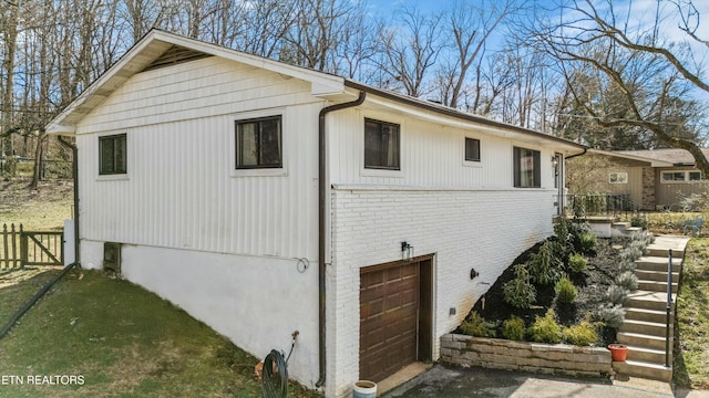 view of property exterior with a garage, brick siding, fence, and driveway