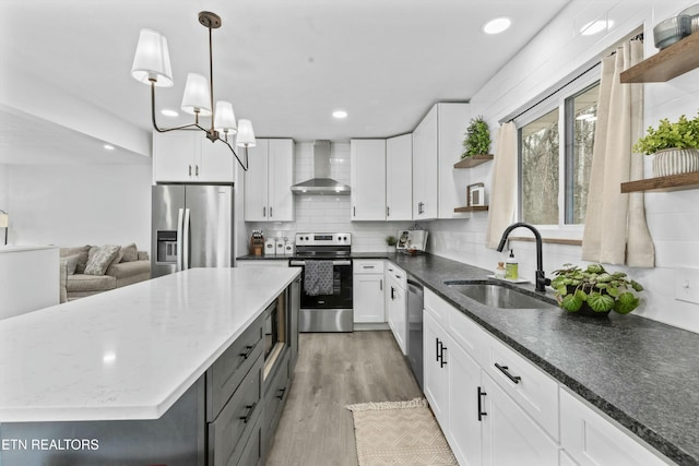 kitchen featuring wall chimney range hood, appliances with stainless steel finishes, open shelves, and a sink