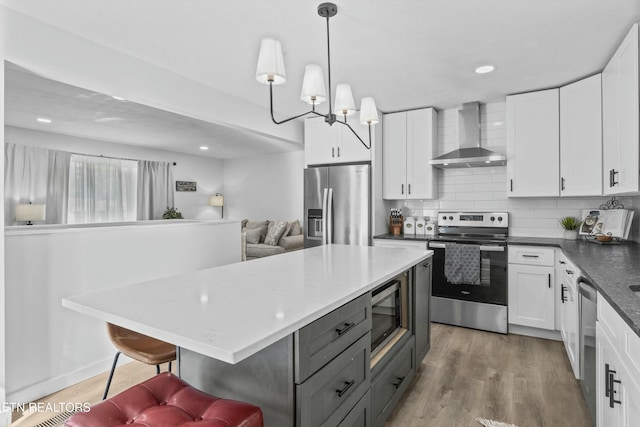 kitchen with wall chimney exhaust hood, white cabinetry, stainless steel appliances, and light wood-style flooring