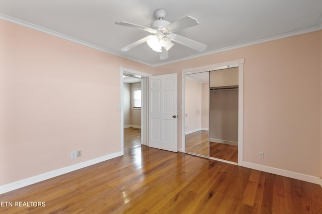 unfurnished bedroom with baseboards, a closet, wood finished floors, and crown molding