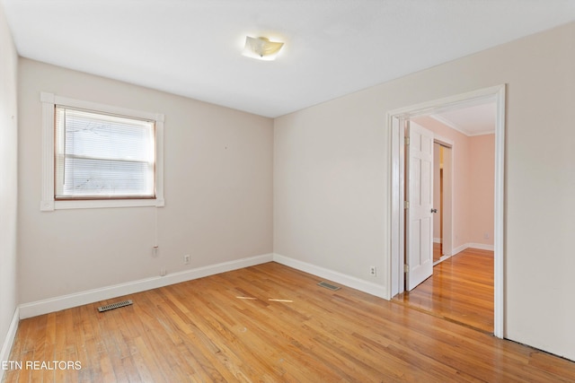 spare room with light wood-type flooring, visible vents, and baseboards