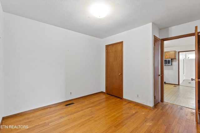 unfurnished bedroom with light wood finished floors, baseboards, visible vents, a textured ceiling, and a closet