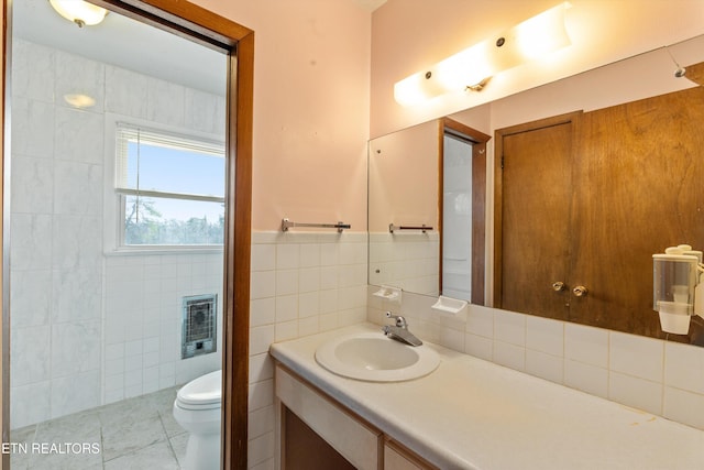 bathroom featuring toilet, tile patterned floors, heating unit, vanity, and tile walls