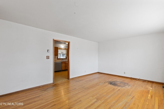 spare room featuring baseboards, a sink, and light wood-style floors